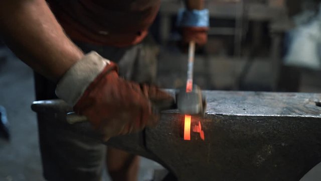 a blacksmith uses a hand hammer on an anvil to forge a red hot metal product