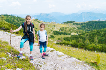 Fototapeta na wymiar Children hiking on beautiful summer day in alps mountains Austria, resting on rock and admire amazing view to mountain peaks. Active family vacation leisure with kids.Outdoor fun and healthy activity.