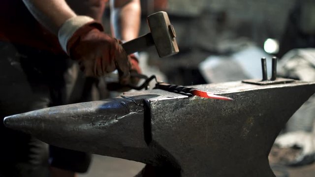 a blacksmith uses a hand hammer on an anvil to forge a red hot metal product