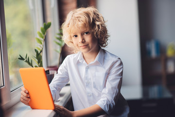 Cute blonde boy holding a tablet and looking thoughtful