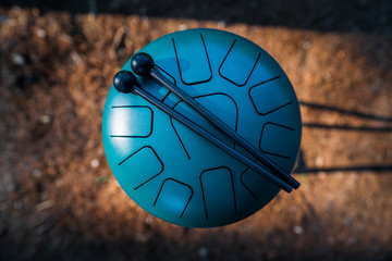 Contemporary green hand pan steel tongue drum musical instrument and a pair of black drum sticks placed on it. Relaxing and healing sounds, music therapy.