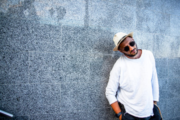 Portrait of stylish handsome man with a beard dressed white t-shirt, black sunglasses,  jeans with bagpack posing against the urban wall in the city on the street