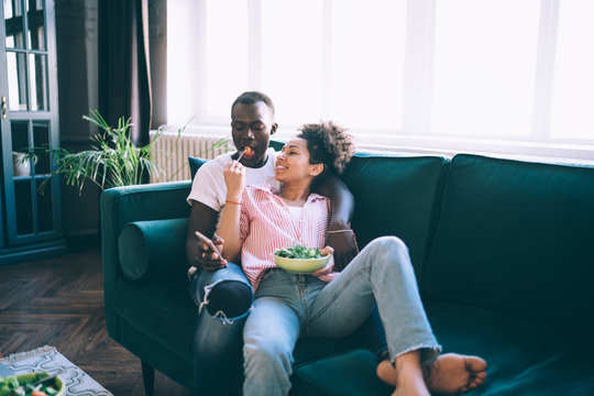 Young casual multiethnic couple enjoying in delicious salad on couch