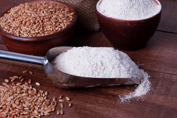 Scoop and bowl with wholegrain flour powder, wheat grains on brown wooden table. High angle, closeup. Harvest, food, ingredient, baking concept