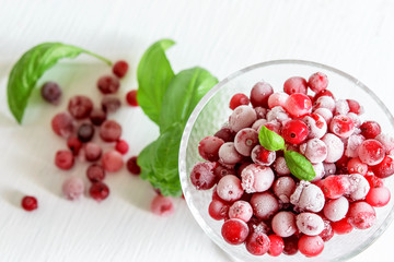 Frozen cranberries in glass bowl on the white table, top view. Frozen food, conservation concept.