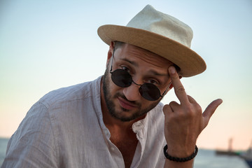 Handsome man with beard relaxing on the street  parapet, smoking ciggarette, drinking and looking to the view of the sea