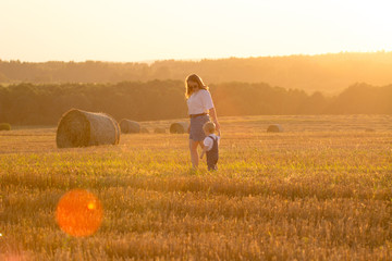 Happy mother and son walk in a field harvested in summer with bales of hay in the background. Summer sunset. Family walk in the field © istorik