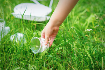 Little girl cleans plastic utensils on the green grass in the park