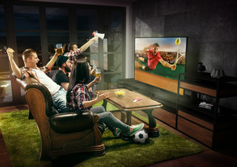 Group of friends watching tennis match, sport together. Emotional men and women cheering for...