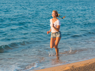 Smiling adult woman in white T-shirt is jogging on the beach near the ocean.