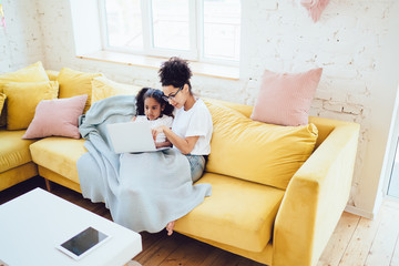 Fototapeta premium Ethnic mother and daughter with laptop on sofa