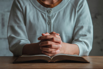 Woman praying, hands clasped together on her Bible. copy space.