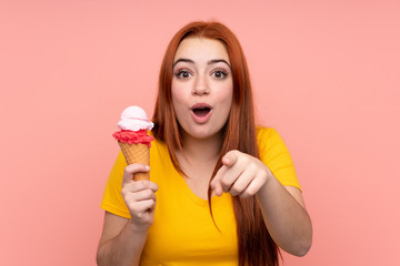 Young girl with a cornet ice cream over isolated background surprised and pointing front