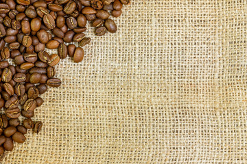 Roasted arabica coffee beans sprinkled on burlap with copy space.