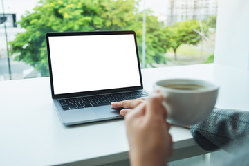 Mockup image of a hand using and touching on laptop touchpad with blank white desktop screen in office