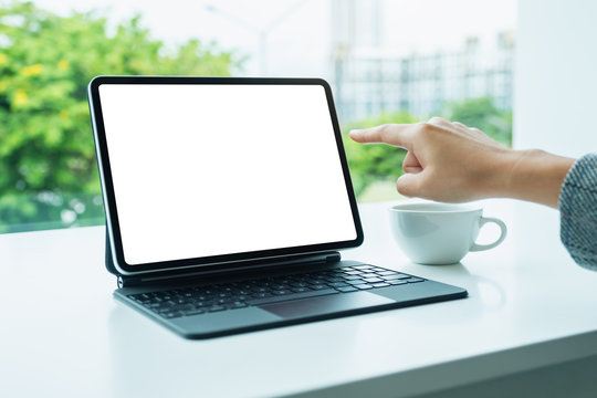 Mockup image of a woman using and pointing finger at digital tablet with blank desktop white screen as a computer pc in office