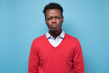 Worried suspicious young african man isolated against blue studio wall