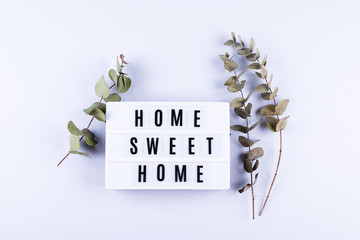 Home Sweet Home Text Light box letters Top view Flat Lay with eucalyptus flower on grey background.