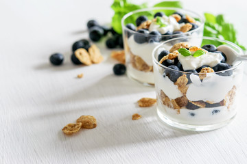 Homemade granola in glasses with yogurt and bluberries on the white. Copy space, healthy food concept.