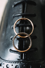 Two gold wedding rings on a background of black men's shoes with lacing.