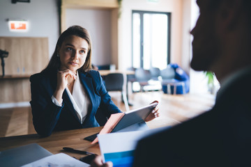 Serious young secretary listening to anonymous male boss attentively in office