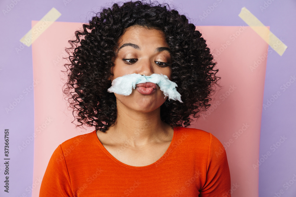 Wall mural Image of amusing african american woman making fun with cotton candy