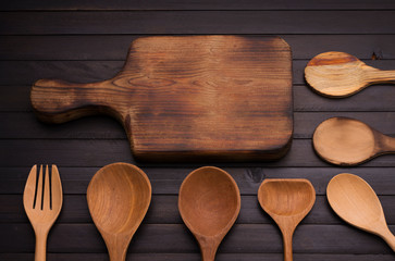 An empty old wooden cutting board with a spoon and fork arranged on an old black wooden table - top view.