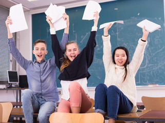 Group portrait of cheerful teen students in auditorium delighted with successful exam results