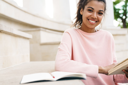 Image of african american student girl reading book while sitting