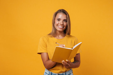 Image of young happy woman smiling and writing in exercise book