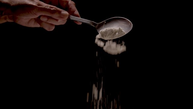 Flour being poured off a tablespoon on a black backdro