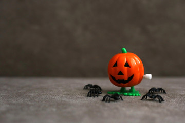 Clockwork toy in the shape of Jack o lantern next to spiders on brown background. Halloween concept