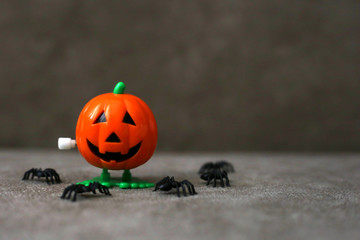 Clockwork toy in the shape of Jack-o- lantern next to spiders on brown background. Halloween concept