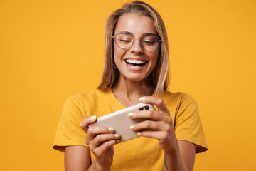 Fototapeta premium Image of smiling woman in eyeglasses playing online game on cellphone