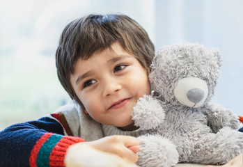 High key light portrait cute boy laying his head on teddy bear and looking out with beautiful brown...