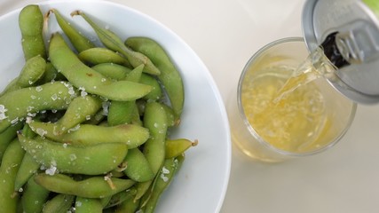 Top view of pouring soda from can to glass. Edamame beans in a bowl. Vegan Japanese snacks