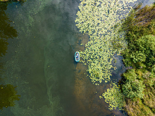 Aerial drone view. Fishing boat on green water near the shore. Algae bloom in the river, green pattern on the water.