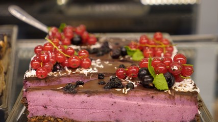 Close up of raw vegan cake decorated with berries on a display in vegan confectionery shop. 