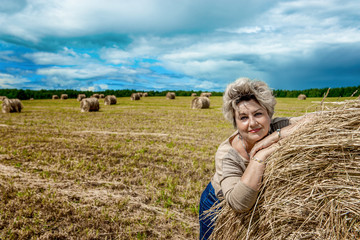 Mature beautiful woman with a bouquet of wild flowers on a mown wheat field. Active recreation, perfect maturity