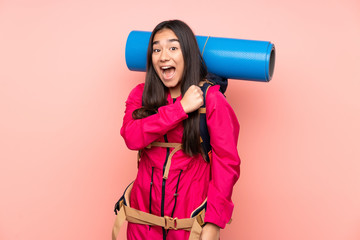 Young mountaineer Indian girl with a big backpack isolated on pink background celebrating a victory