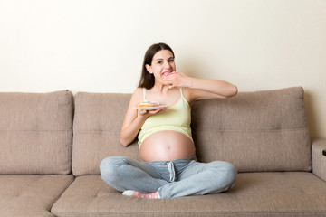 Pregnant woman is eating many donuts relaxing on the sofa. Unhealthy dieting during pregnancy concept