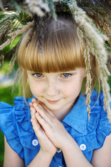 beautiful red-haired girl with freckles and a wreath of summer herbs on her head looks into the camera with blue eyes. Young beautiful girl 7-10 years old in nature