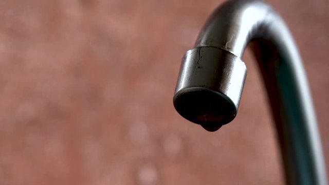 The old tap on the kitchen mixer is leaking. Tap water dripping. Daylight macro photography.