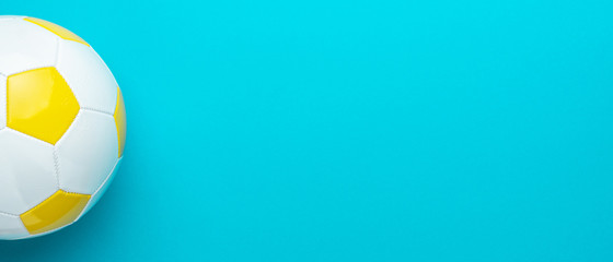 Top view of part of white and yellow soccer ball over turquoise blue background with copy space. Minimalist flat lay image of football ball as sport background.