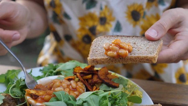 Female putting beans on a slice of brown bread with a fork. Full English breakfast consist of scramble, mushrooms and vegetables. Healthy lifestyle concept