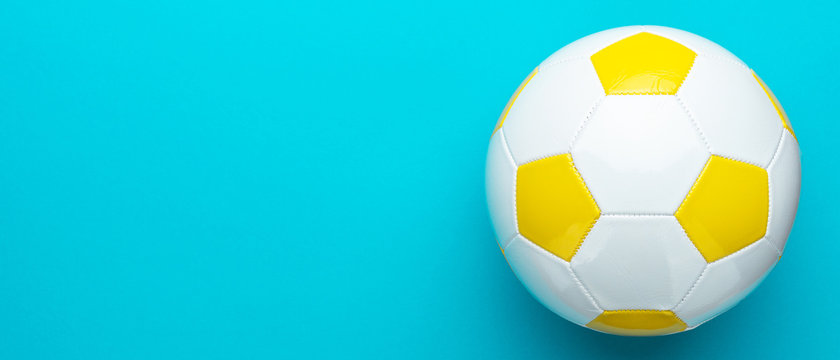 Top view photo of white and yellow soccer ball as football concept . Minimalist flat lay image of leather football ball over blue turquoise background with copy space and right side composition.