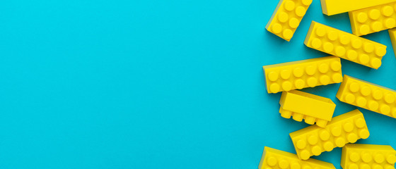 Top view of yellow plastic blocks. Right side composition of yellow building blocks from child constructor. Bright plastic blocks on turquoise blue background with copy space.