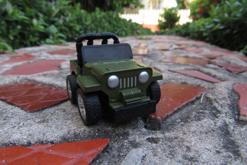 Closeup of a green car toy on the ground in a garden under the sunlight