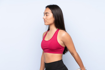 Fototapeta premium Young Indian sport woman isolated on blue background stretching leg