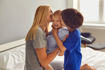 Mother and children hug and kiss on the bed in the room. Mothers Day. Mom and sons cuddle up.